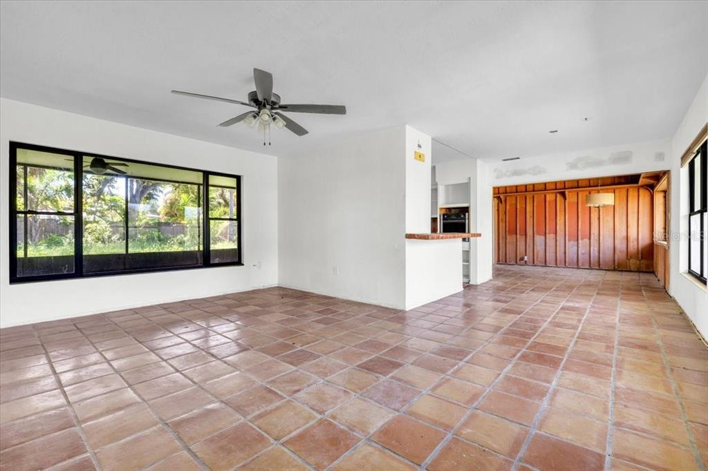 A living room with terracotta tile flooring, a ceiling fan, and a wood-paneled adjacent room — 807 LUCILLE AVENUE, NOKOMIS, FL