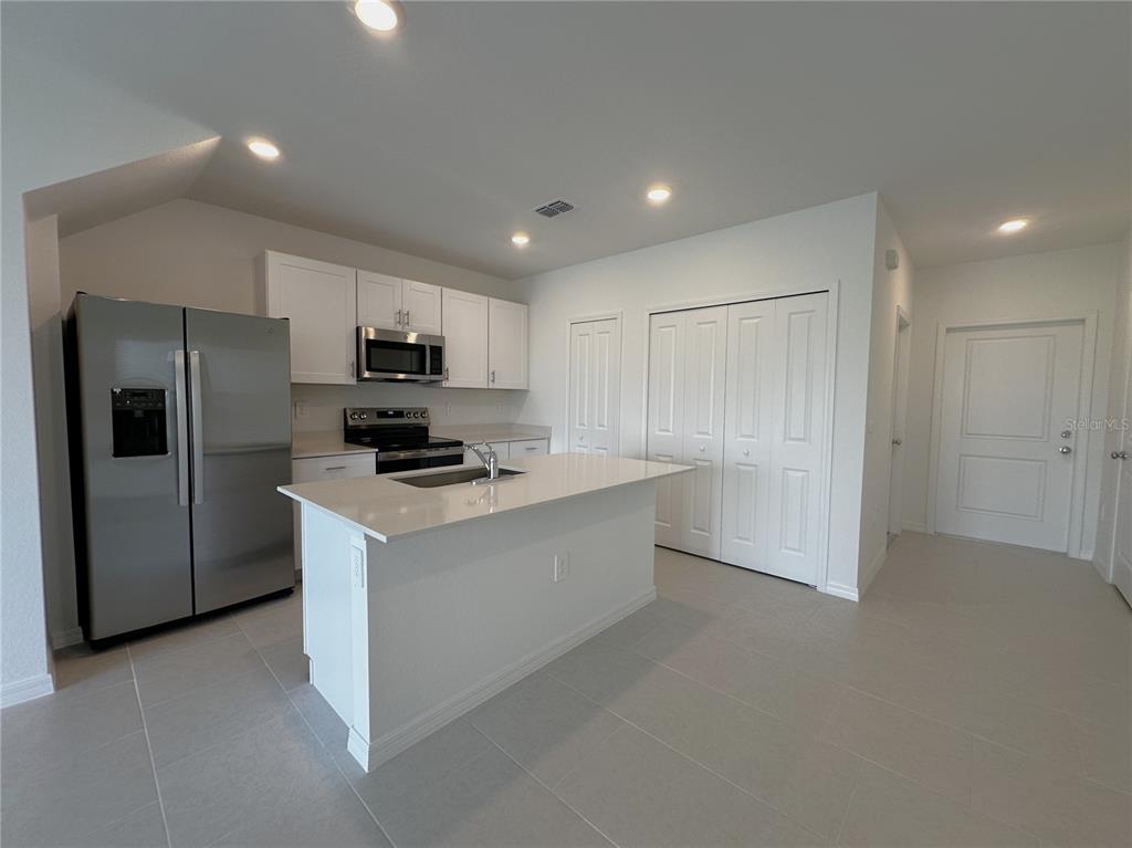 A modern kitchen features white cabinets, stainless steel appliances, a center island, and tile flooring — 28521 SWEET MEADOW DRIVE, PUNTA GORDA, FL