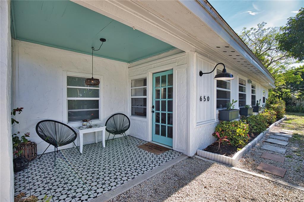 A covered porch features a patterned tile floor, two black chairs, and a teal door — 650 EDWARDS STREET, ENGLEWOOD, FL