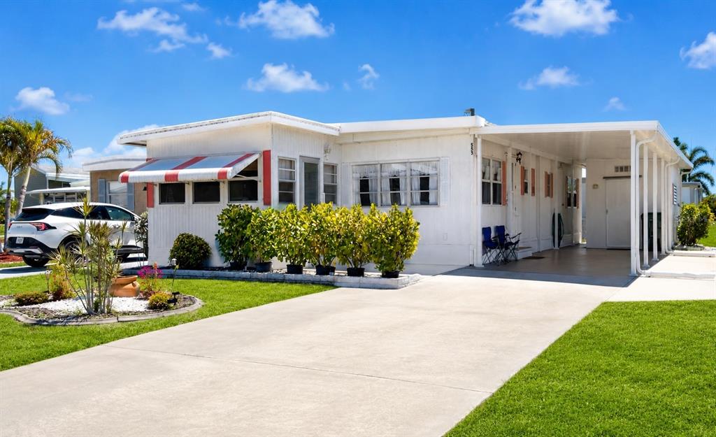 A white manufactured home features a red-and-white striped awning, a carport, and a landscaped yard — 553 FLEETWOOD STREET, NORTH PORT, FL