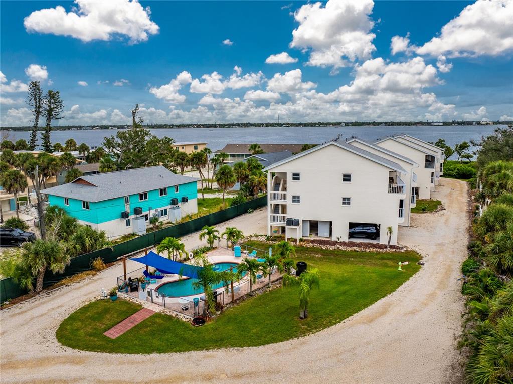 An aerial view shows two multi-story buildings, a swimming pool with a blue shade sail, and water — 5031 N BEACH ROAD UNIT 222, ENGLEWOOD, FL