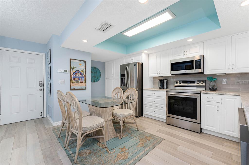 A kitchen and dining area with white cabinets, stainless steel appliances, and a glass table — 5031 N BEACH ROAD UNIT 222, ENGLEWOOD, FL