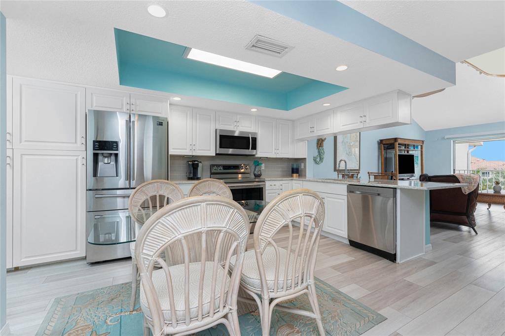 A kitchen features white cabinetry, stainless steel appliances, and a bright blue recessed ceiling — 5031 N BEACH ROAD UNIT 222, ENGLEWOOD, FL