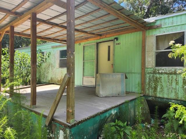 An exterior view of a weathered mobile home with a wooden porch and metal roof — 3140 NE 162ND PLACE, CITRA, FL