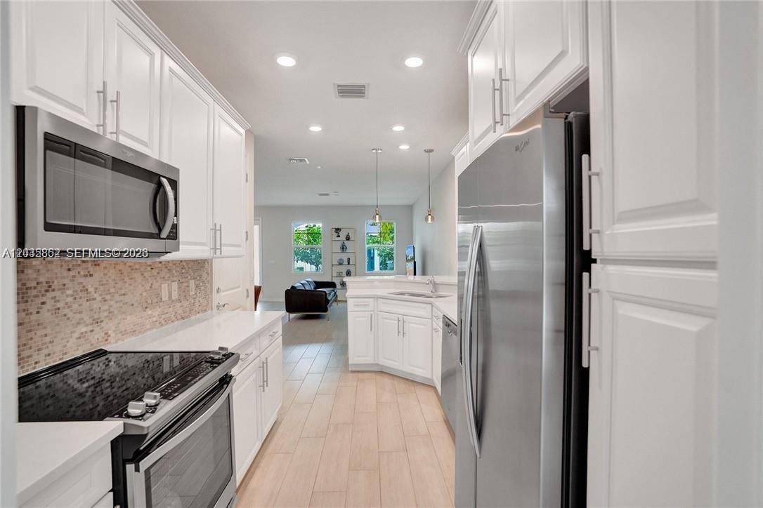 A galley-style kitchen features white cabinets, stainless steel appliances, and a tiled backsplash — 5140 Eucalyptus Dr # 5, Hollywood FL 33021, HOLLYWOOD, FL