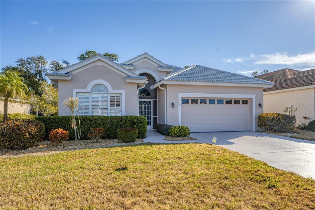 A single-story house with a beige stucco exterior, a tiled roof, and a two-car garage — 711 BACK NINE DRIVE, VENICE, FL
