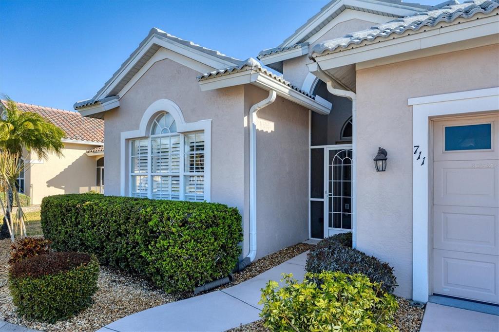 The exterior of a beige house features a front door, a window, and landscaping — 711 BACK NINE DRIVE, VENICE, FL