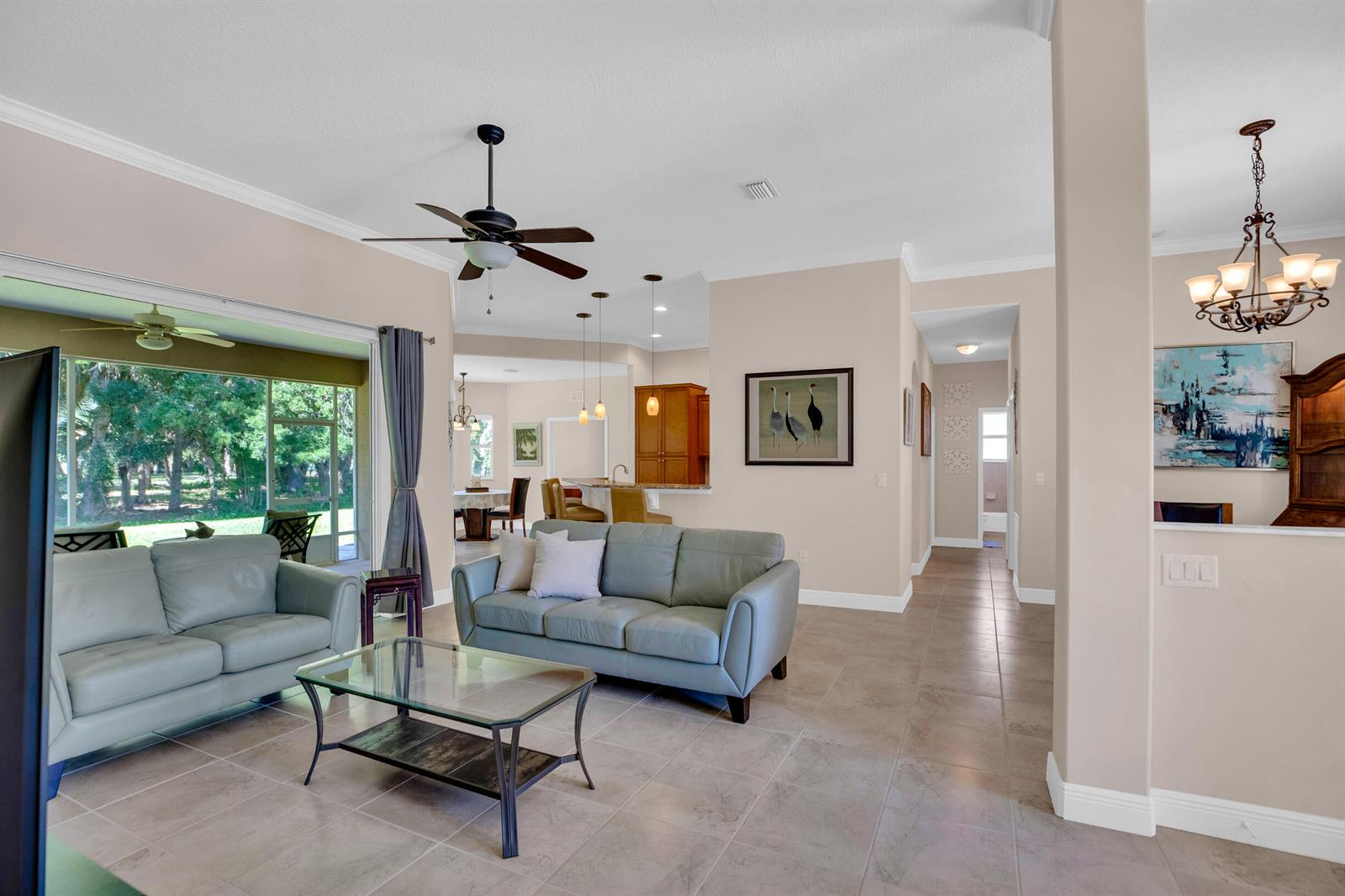 A living room with light-colored tile floors, two leather sofas, and an open kitchen view — 7445 36th Court, Vero Beach FL 32967, VERO BEACH, FL