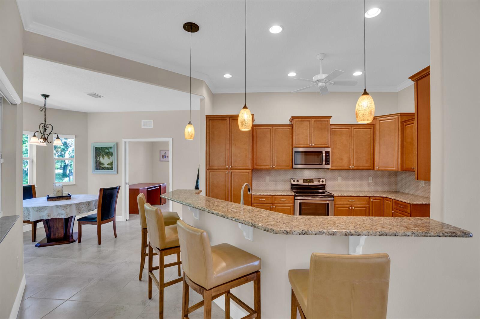 A kitchen with wood cabinets and granite countertops features a breakfast bar with three stools — 7445 36th Court, Vero Beach FL 32967, VERO BEACH, FL