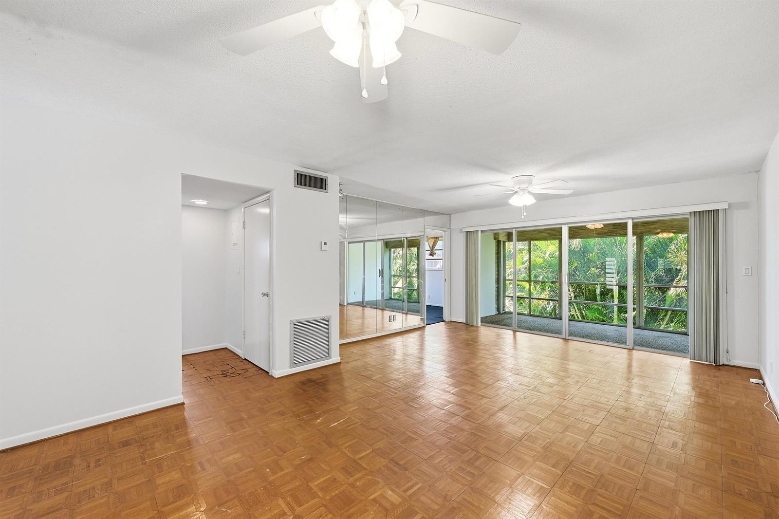 A living room with parquet wood flooring, mirrored walls, and sliding glass doors to a balcony — 2160 NE 36th Street # 37, Lighthouse Point FL 33064, LIGHTHOUSE POINT, FL