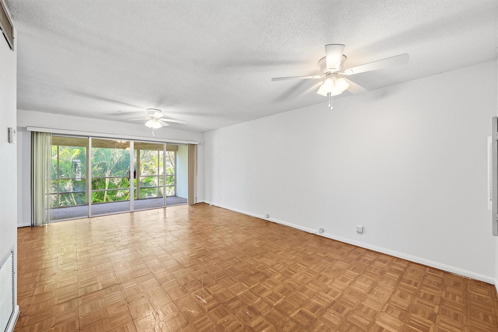 An empty living room features parquet wood flooring, white walls, two ceiling fans, and sliding doors — 2160 NE 36th Street # 37, Lighthouse Point FL 33064, LIGHTHOUSE POINT, FL