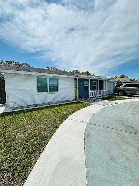 A white brick, single-story house features a blue front entrance and a curved concrete driveway — 6310 WESTPORT DRIVE, PORT RICHEY, FL