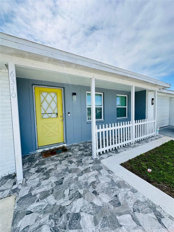 A house exterior features a yellow front door, blue siding, and a stone-patterned porch floor — 6310 WESTPORT DRIVE, PORT RICHEY, FL