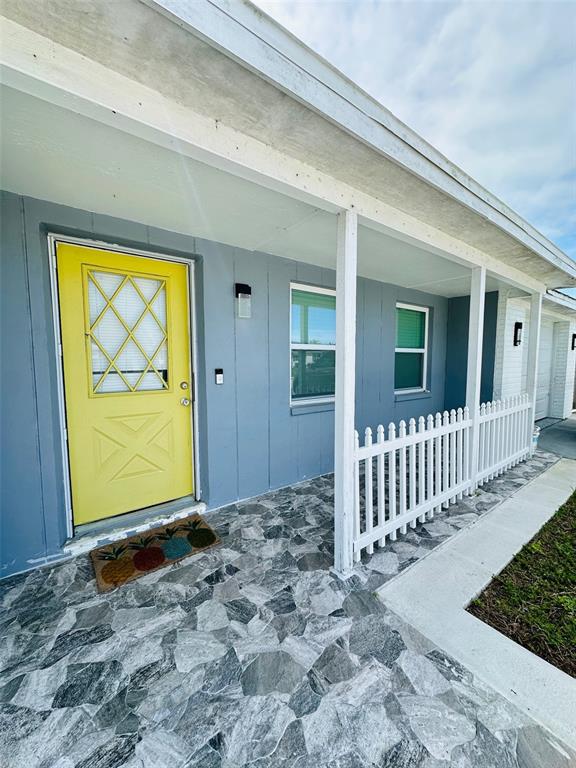 A house exterior features a yellow front door, gray siding, and a stone-patterned porch floor — 6310 WESTPORT DRIVE, PORT RICHEY, FL