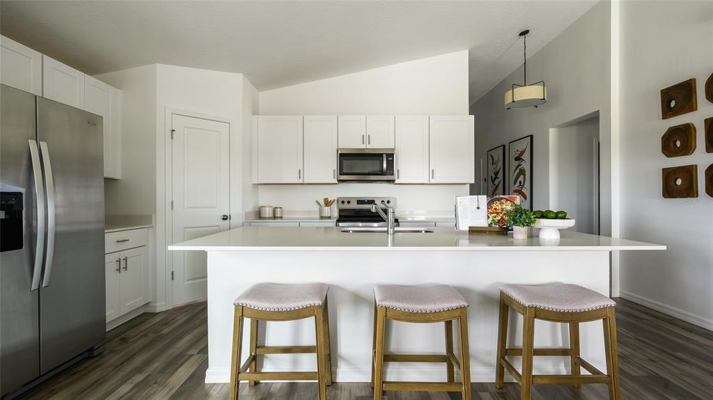 A kitchen features white cabinets, a large island with three stools, and stainless steel appliances — 3907 ALTITUDE RUN, DAVENPORT, FL
