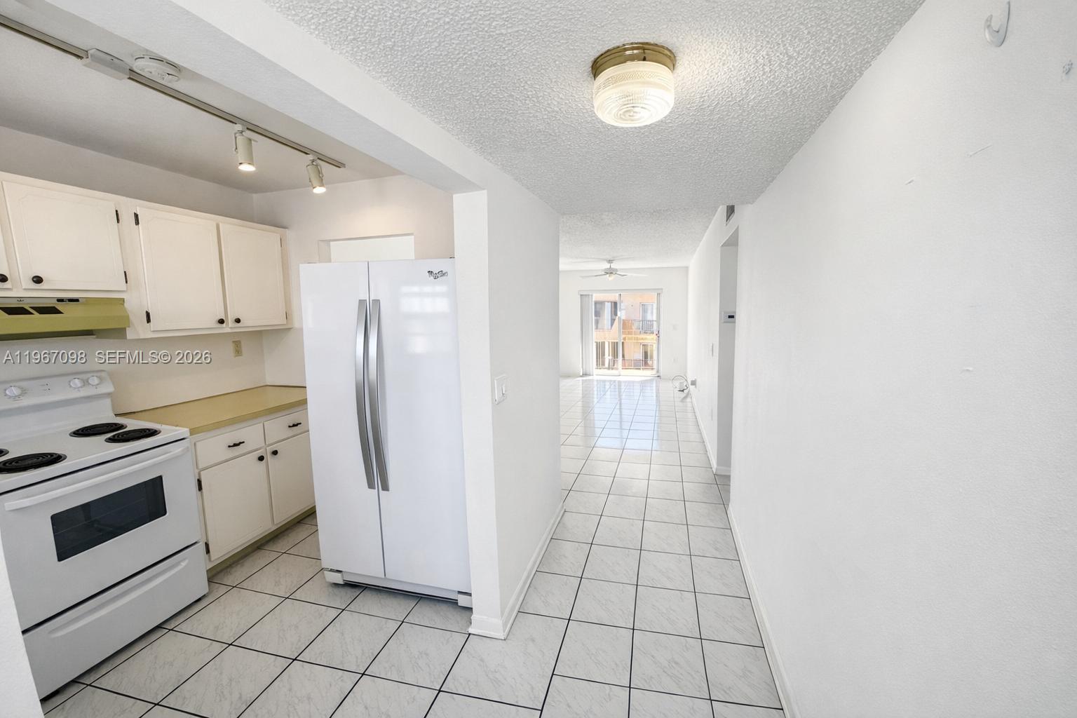A white kitchen with a refrigerator and stove opens into a tiled living area — 1630 W 46th St # 514B, Hialeah FL 33012, HIALEAH, FL