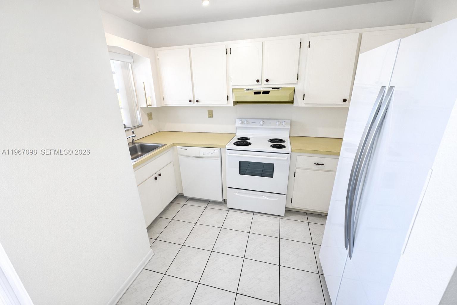 A kitchen features white cabinets, white appliances, a yellow countertop, and light-colored tile flooring — 1630 W 46th St # 514B, Hialeah FL 33012, HIALEAH, FL