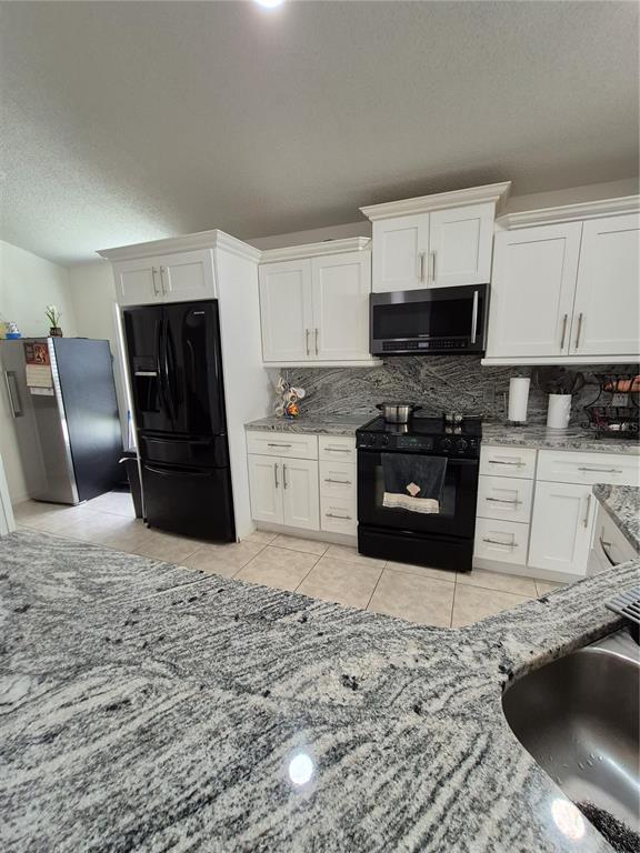 A kitchen features white cabinets, black appliances, and gray granite countertops — 3114 STERN COURT, KISSIMMEE, FL