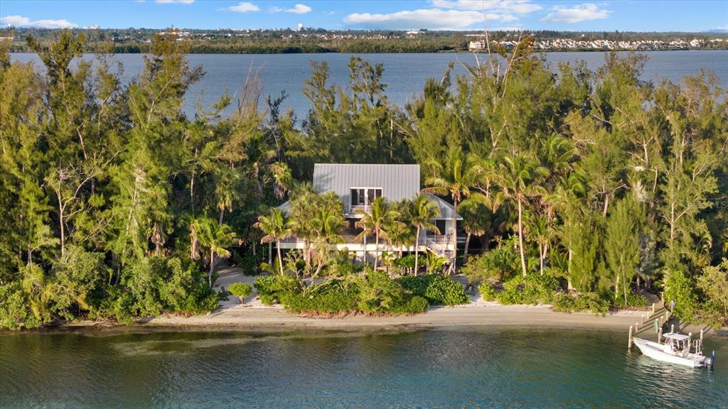 An aerial view shows a house nestled in a wooded area beside a turquoise bay — 7143 LA LENAIRE DRIVE, LONGBOAT KEY, FL