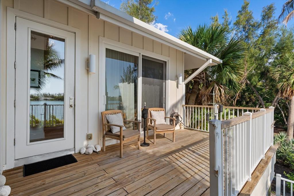 A screened-in wooden porch features outdoor furniture overlooking a blue bay and palm trees — 7143 LA LENAIRE DRIVE, LONGBOAT KEY, FL