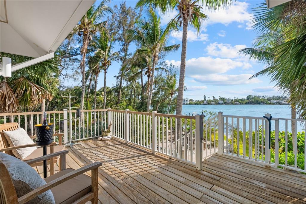 A screened-in porch with wood furniture overlooks a tropical waterfront view with palm trees — 7143 LA LENAIRE DRIVE, LONGBOAT KEY, FL