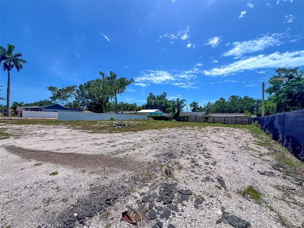 A vacant, gravel-covered lot is enclosed by a fence under a bright blue sky — 35TH STREET W, BRADENTON, FL