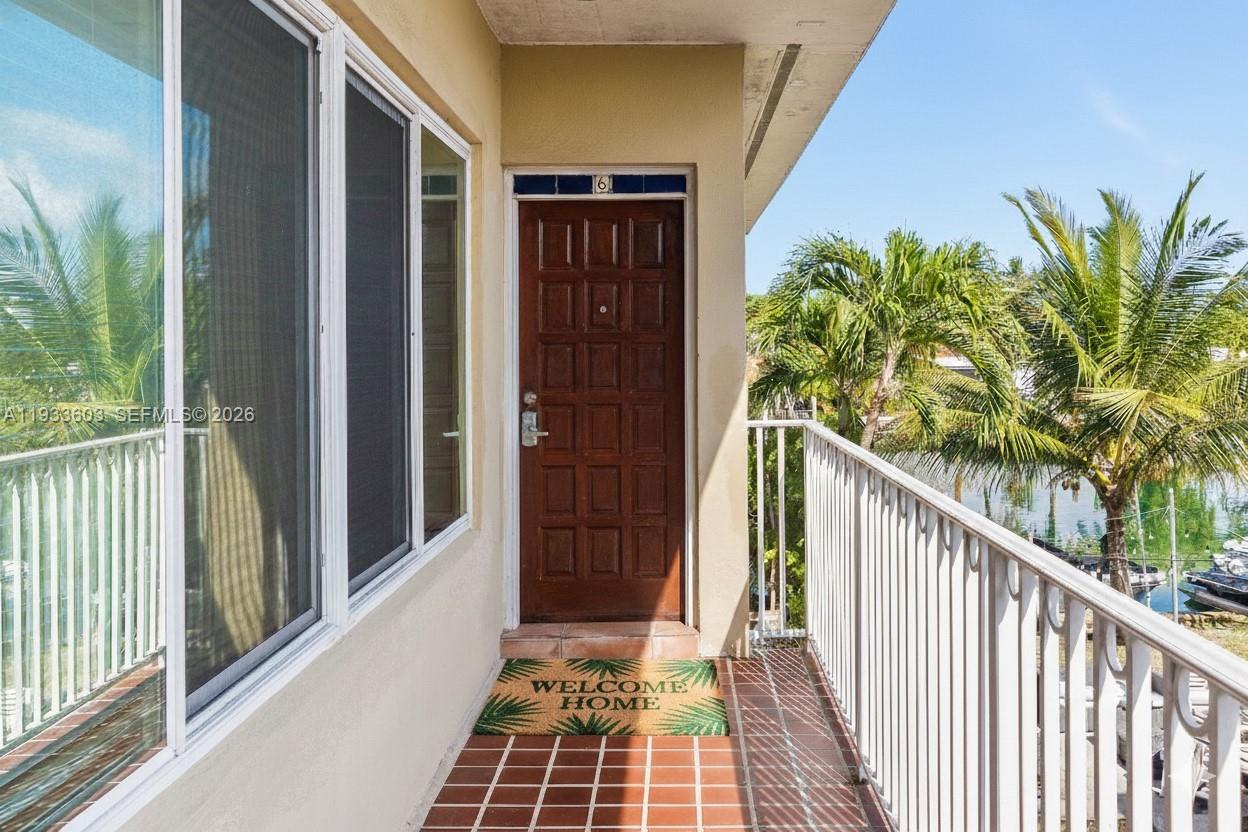An outdoor balcony features a brown door, tiled flooring, and a white metal railing — 1925 Calais Drive # 6, Miami Beach FL 33141, MIAMI BEACH, FL