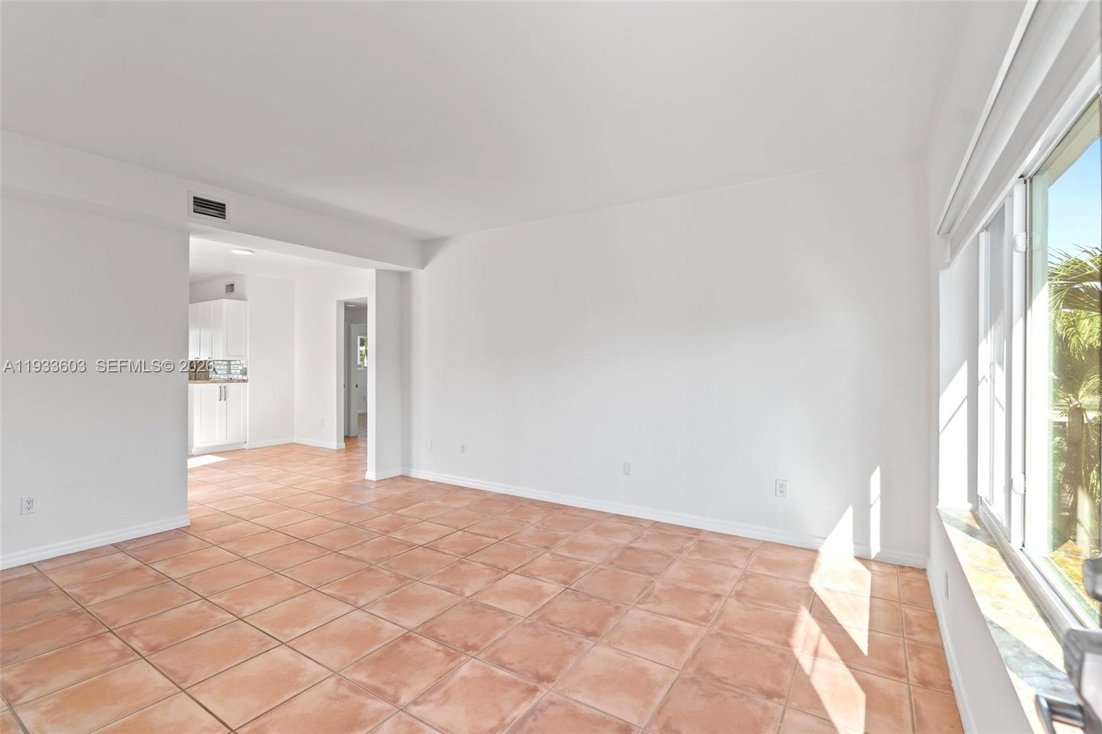 A bright, empty room features white walls, terracotta tile flooring, and a large window — 1925 Calais Drive # 6, Miami Beach FL 33141, MIAMI BEACH, FL
