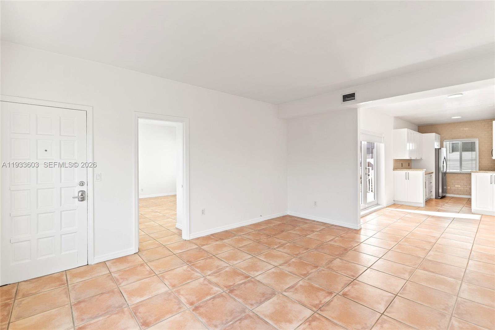 An open living area features white walls, tan tile flooring, and an adjacent kitchen — 1925 Calais Drive # 6, Miami Beach FL 33141, MIAMI BEACH, FL