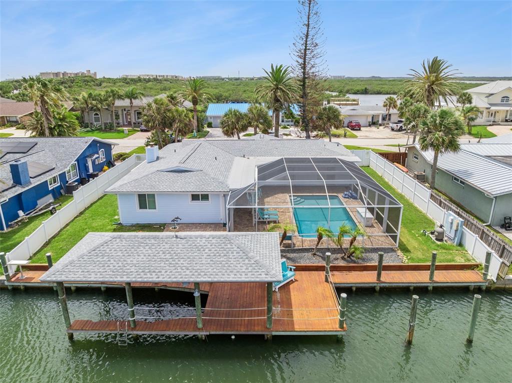 An aerial view of a waterfront house with a pool, screened enclosure, and wooden dock — 106 ANCHOR DRIVE, PONCE INLET, FL