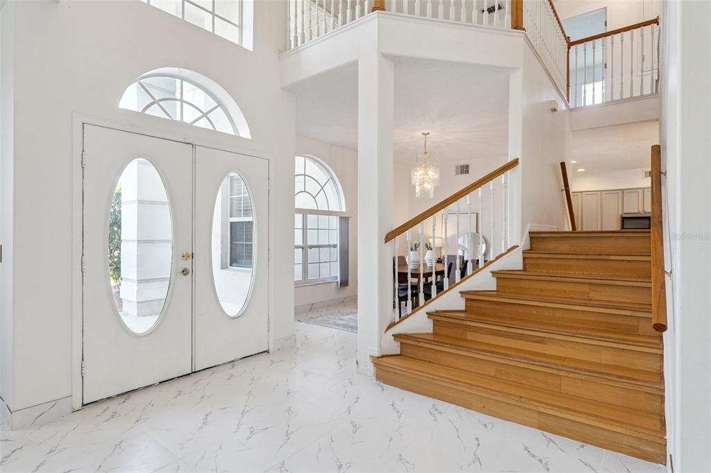 A bright foyer features white marble-look tile floors, a double front door, and wooden stairs — 2205 WINTERMERE POINTE DRIVE, WINTER GARDEN, FL