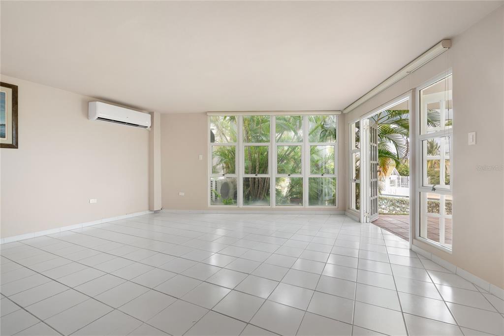 A bright, empty room features white tile flooring, a wall-mounted air conditioner, and large windows — 125 PALMARINA CLUB UNIT 12, HUMACAO, PR