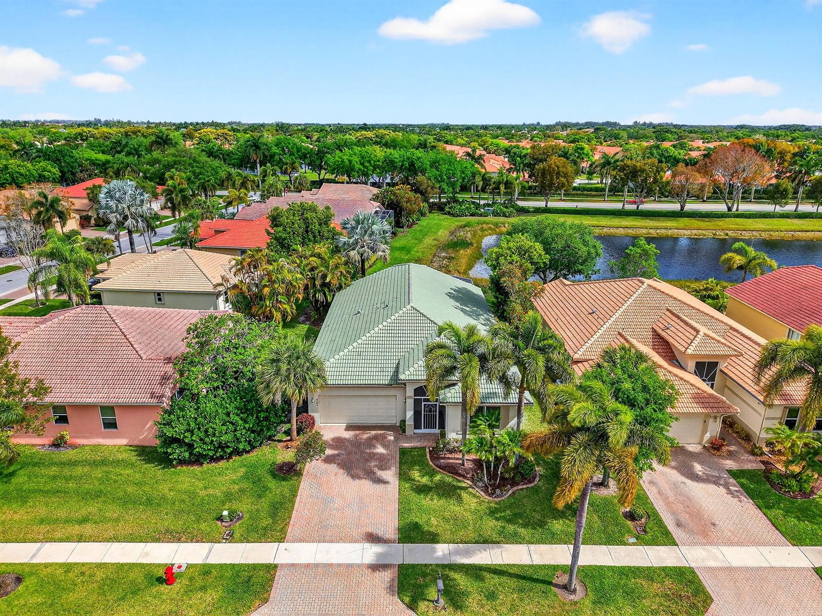 An aerial view shows a suburban house with a green roof and palm trees — 8706 Bellido Circle, Boynton Beach FL 33472, BOYNTON BEACH, FL