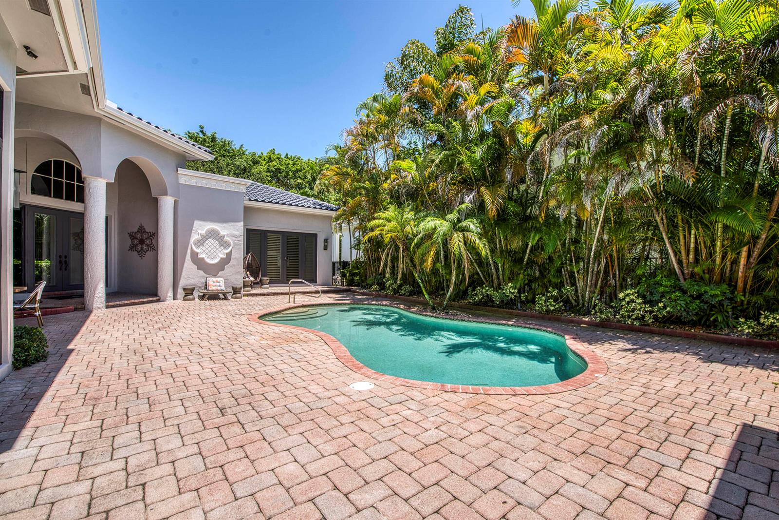 A backyard patio features a kidney-shaped swimming pool surrounded by brick pavers and palm trees — 16340 Via Venetia E, Delray Beach FL 33484, DELRAY BEACH, FL