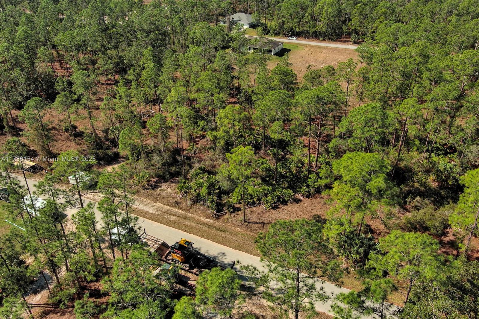 An aerial view shows a wooded lot with a paved road and construction equipment — 2309 Grant Ave, Lehigh Acres FL 33920, LEHIGH ACRES, FL