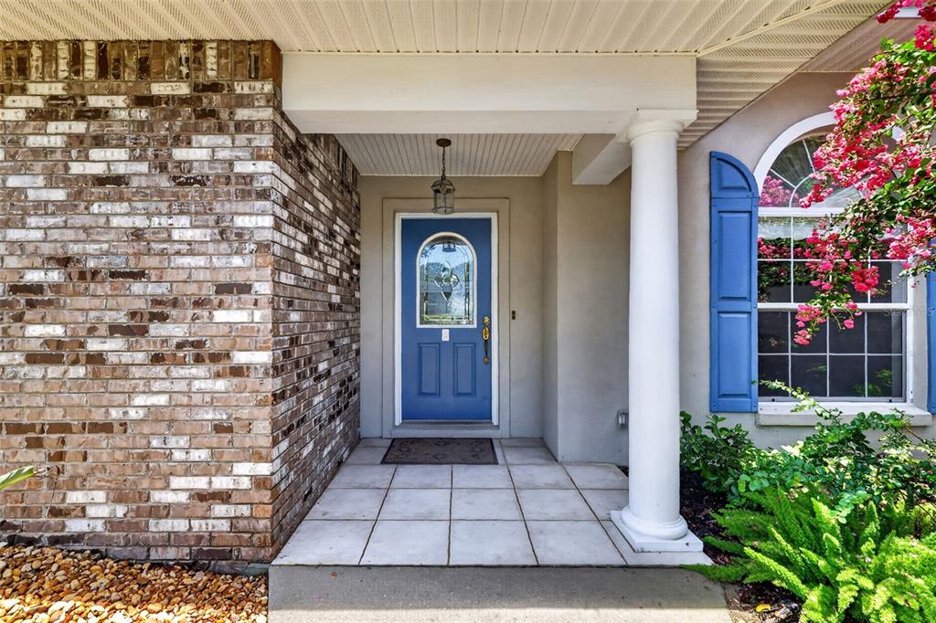 A front porch with a blue door, brick siding, and a white column — 705 HILLTOP COURT, MOUNT DORA, FL