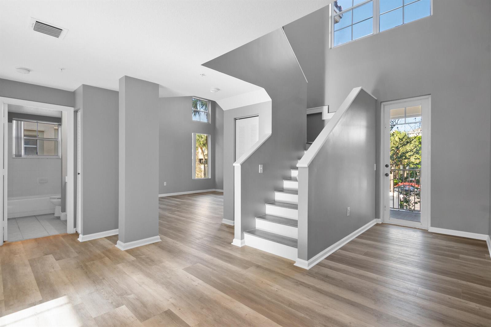 A bright living area features light wood-look flooring, gray walls, and a staircase with white treads — 4822 Chancellor Drive # 20, Jupiter FL 33458, JUPITER, FL
