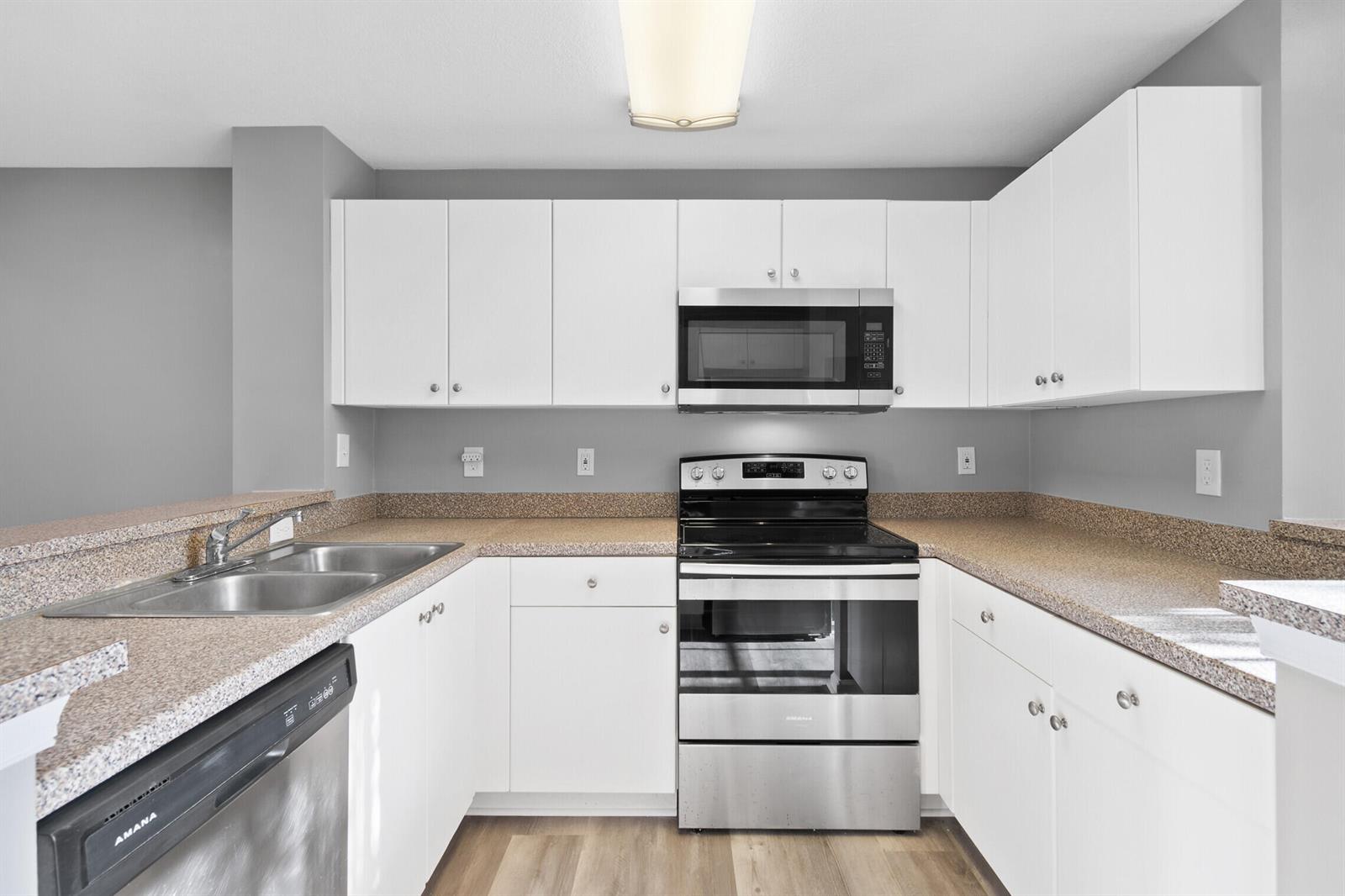 A kitchen features white cabinets, stainless steel appliances, and speckled countertops against gray walls — 4822 Chancellor Drive # 20, Jupiter FL 33458, JUPITER, FL