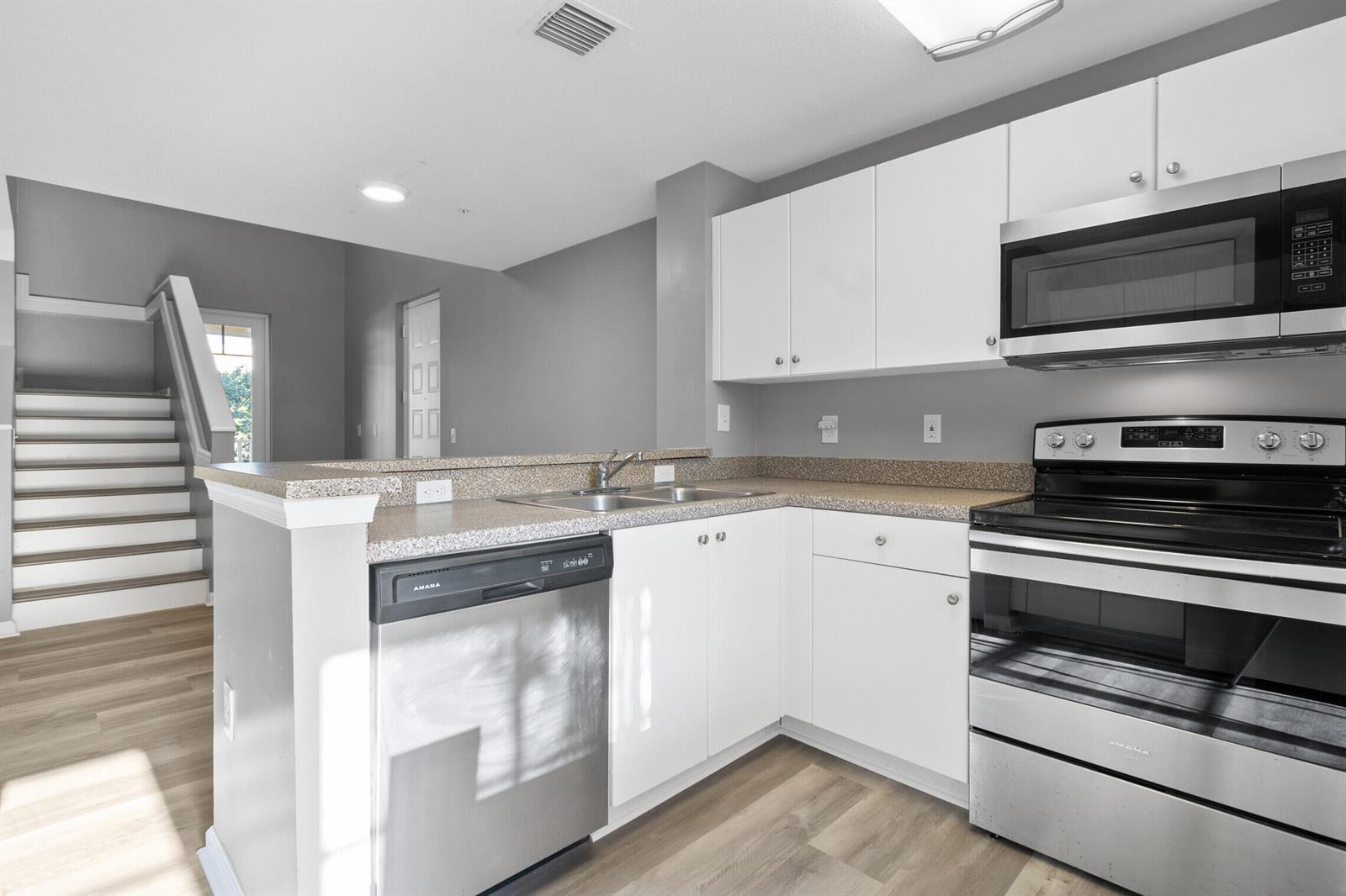 A kitchen with white cabinets, stainless steel appliances, and a breakfast bar overlooks a staircase — 4822 Chancellor Drive # 20, Jupiter FL 33458, JUPITER, FL