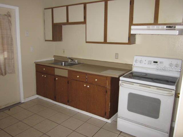 A kitchen features wood cabinets, a stainless steel sink, a white stove, and tiled flooring — 8619 N MULBERRY STREET UNIT A, TAMPA, FL