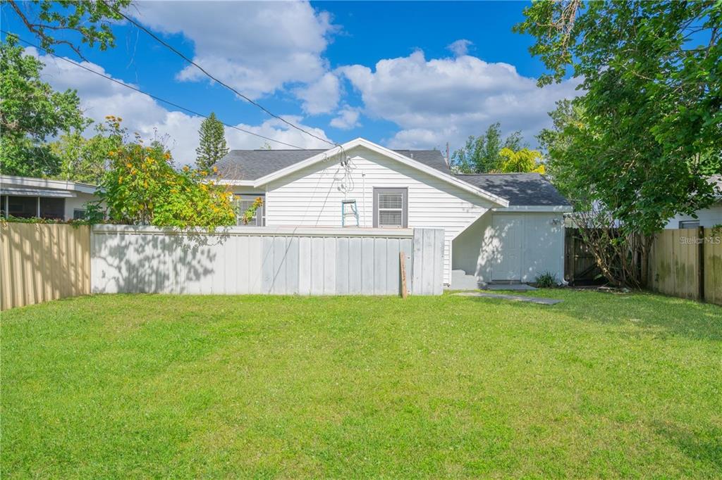 A backyard view of a white-sided house with a fenced lawn and mature trees — 811 OVERSPIN DRIVE, WINTER PARK, FL