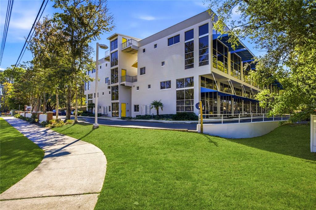 A modern three-story commercial building with blue awnings and large windows next to a parking lot — 2515 SW 35TH PLACE UNIT 117, GAINESVILLE, FL