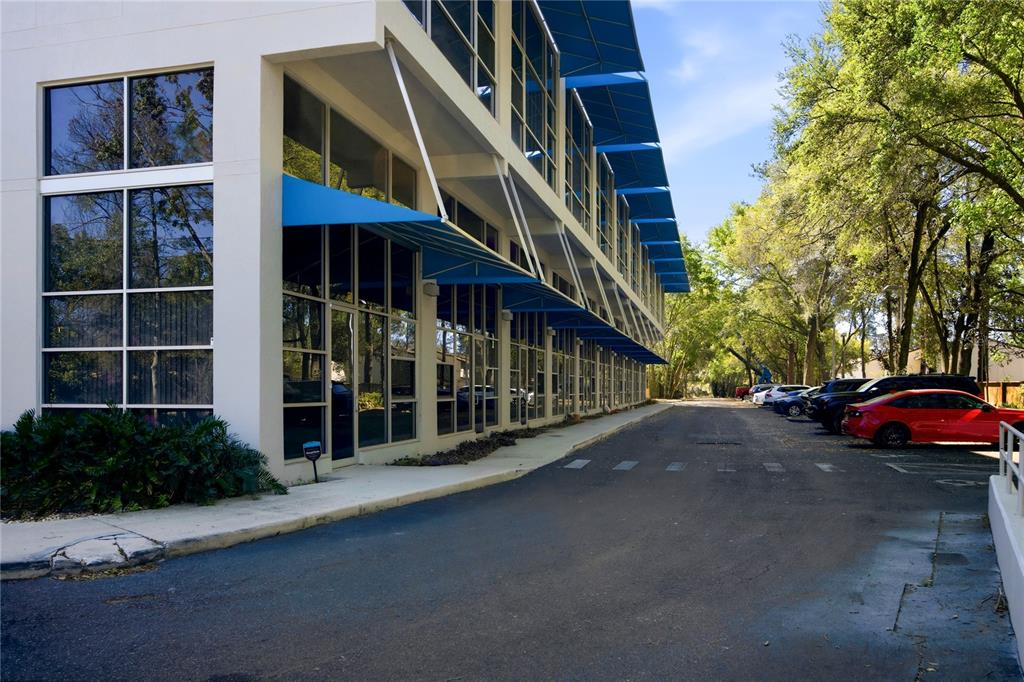 A modern multi-story office building with blue awnings and a parking lot on the right — 2515 SW 35TH PLACE UNIT 117, GAINESVILLE, FL