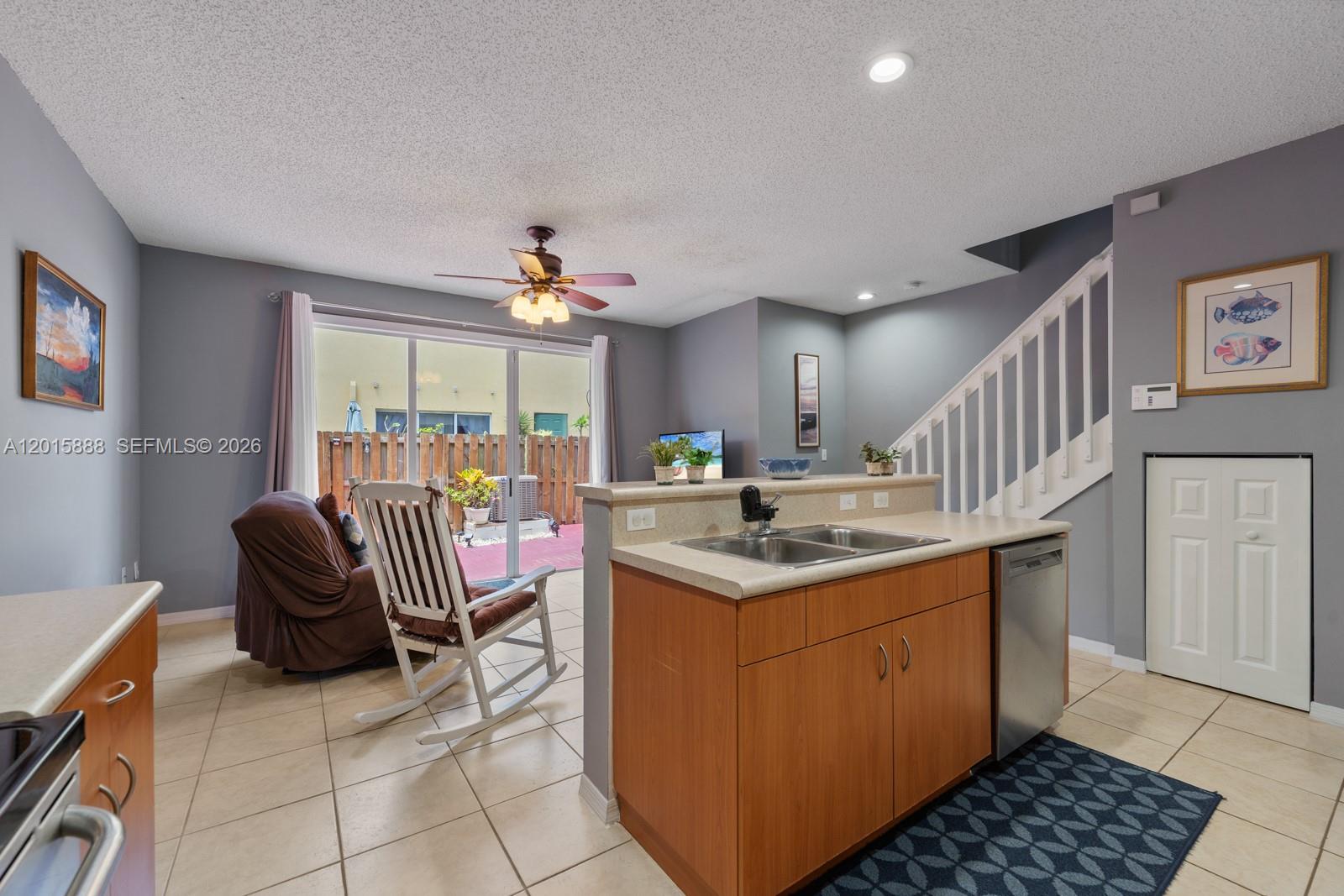 A kitchen with wood cabinets and a stainless steel dishwasher overlooks a living area — 934 NE 42nd Ter, Homestead FL 33033, HOMESTEAD, FL