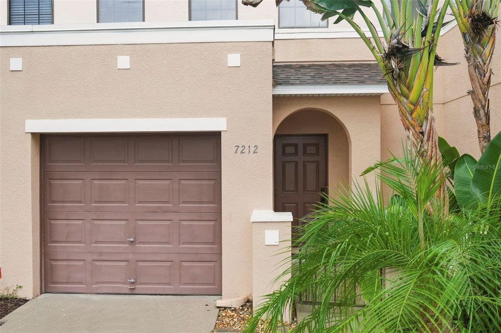 A tan stucco townhouse exterior features a single-car garage and a recessed front entrance — 7212 STERLING POINT COURT, GIBSONTON, FL