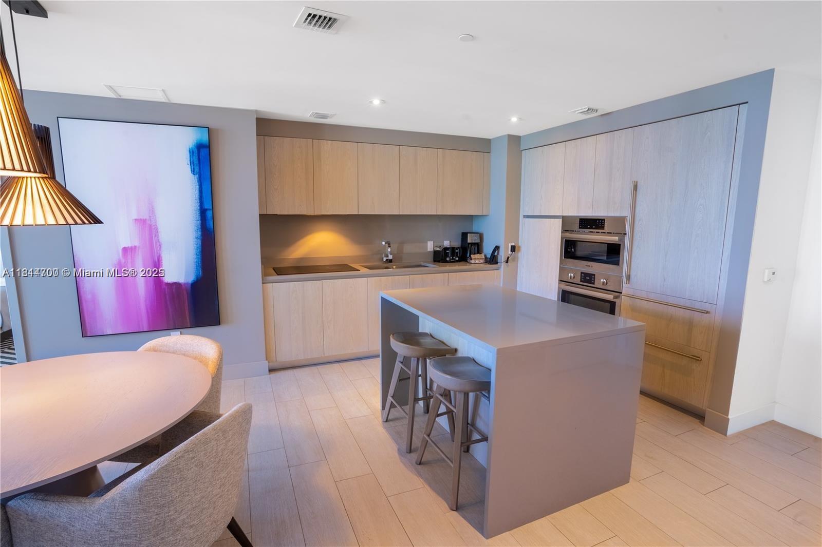 A modern kitchen features light wood cabinetry, a gray island with barstools, and stainless appliances — 4010 S Ocean Dr # R1905, Hollywood FL 33019, HOLLYWOOD, FL