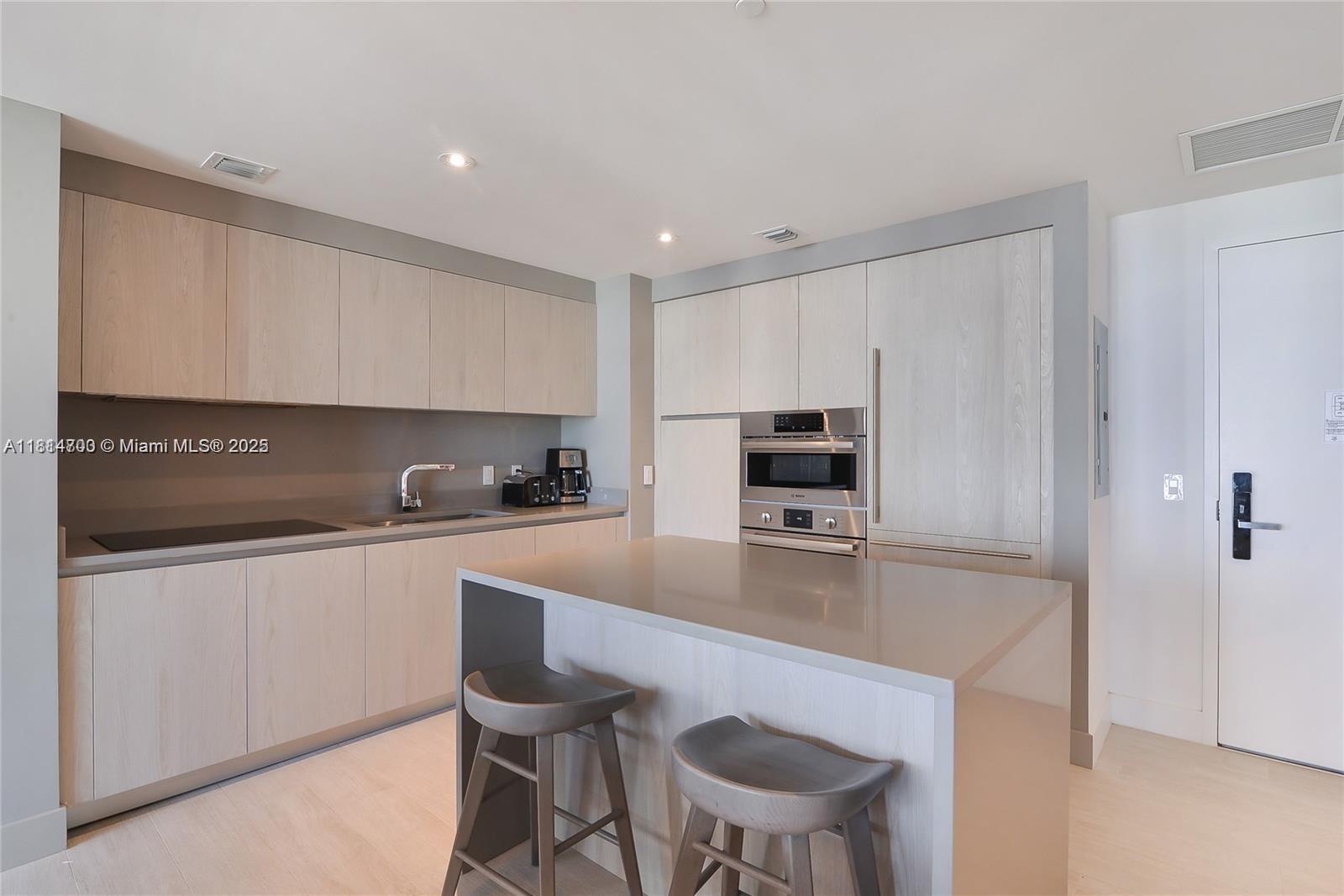 A modern kitchen features light wood cabinetry, a gray island with two stools, and stainless appliances — 4010 S Ocean Dr # R1905, Hollywood FL 33019, HOLLYWOOD, FL
