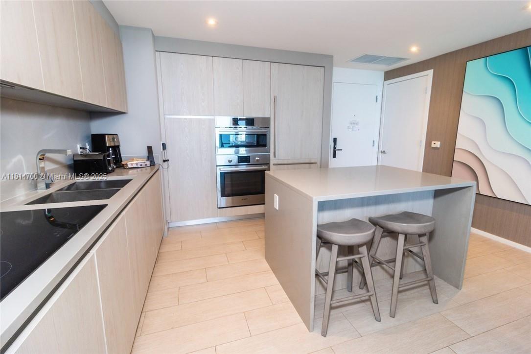 A modern kitchen features light wood cabinetry, stainless steel appliances, and a central island with stools — 4010 S Ocean Dr # R1905, Hollywood FL 33019, HOLLYWOOD, FL