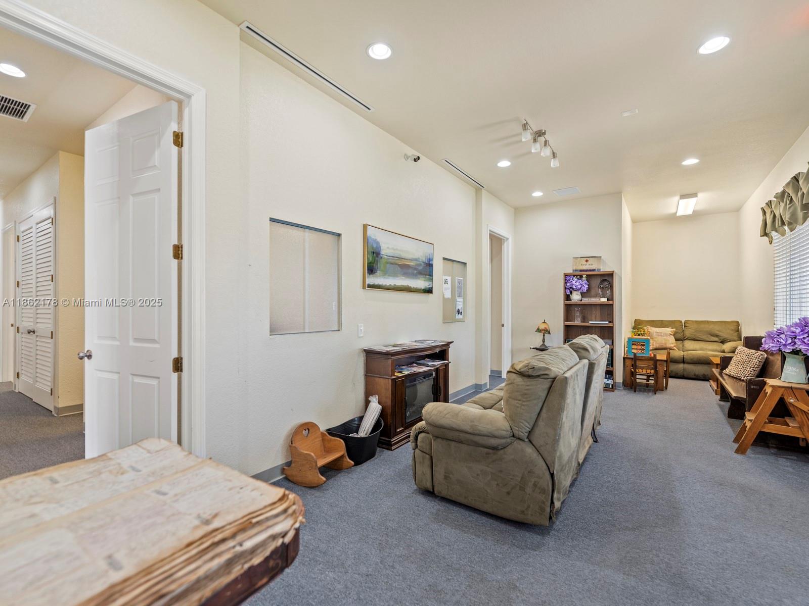 A carpeted waiting room features a recliner, a sofa, a bookshelf, and a fireplace console — 45 NW 4th St, Homestead FL 33030, HOMESTEAD, FL