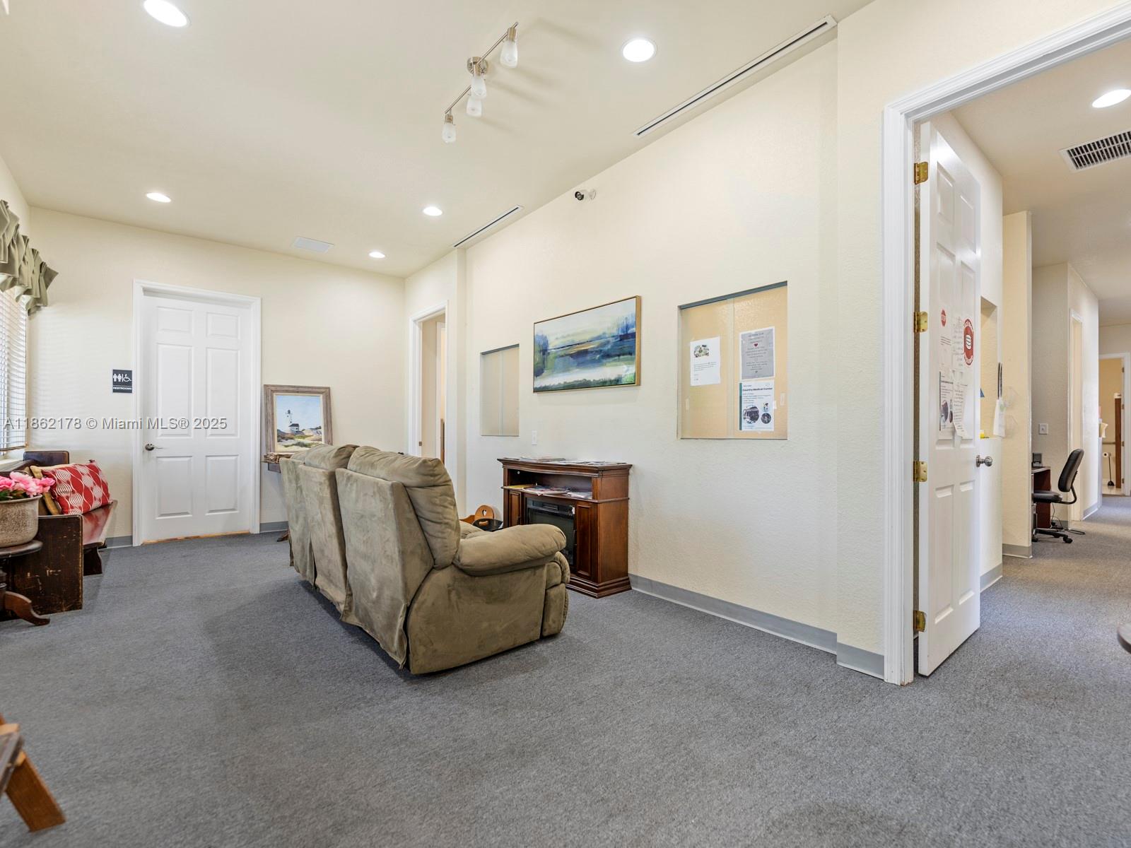 A waiting room features a brown loveseat, gray carpeting, a bulletin board, and white doors — 45 NW 4th St, Homestead FL 33030, HOMESTEAD, FL